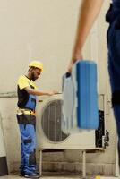 Master serviceman arriving on location to help apprentice worker fix unfunctional compressor in faulty hvac system. Experts coworkers contracted to prevent internal parts breakdowns photo