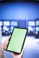 Technical support employee troubleshooting data center servers performance trends. Expert using chroma key tablet to spot high tech facility operational issues causing hardware to slow down photo