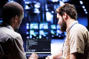 IT developers collaborating in server farm writing script code on laptop terminals. Programmers team conducting maintenance tasks in highly advanced data center, ensuring racks software is up to date photo