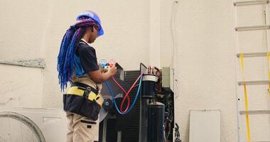 Skilled african american expert looking at freon levels in air conditioner while using manifold indicators to measure the pressure in HVAC system, ensuring efficient cooling performance photo
