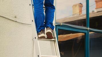 Certified technician holding cordless drill, stepping down from folding ladder after finishing checkup on rooftop condenser. Skilled expert at the end of maintenance assignment photo