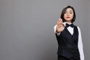 Serious asian waitress showing stop symbol with hand and looking at camera with confident face expression. Catering service woman employee making rejection sign with arm portrait photo