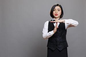 Serious asian waitress showing time out gesture with hands and looking at camera with confident facial expression. Young attractive woman receptionist making interruption symbol portrait photo