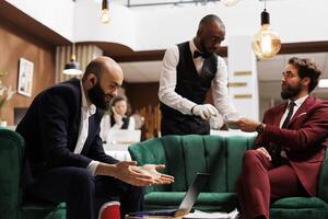 Business person attends online call in lounge area at luxury hotel, using remote videoconference meeting and waiting for check in process. Entrepreneur travelling for work purposes. photo