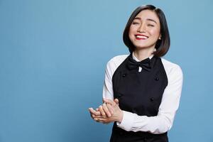 Smiling cafe waitress applauding with joy and encouragement, showcasing appreciation portrait. Attractive woman receptionist clapping hands and laughing while posing in studio photo