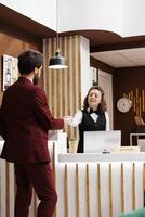 Front desk staff hands out access card for businessman, ensuring comfortable and hassle free stay at luxury hotel. Receptionist with impeccable customer service providing room key after long trip. photo