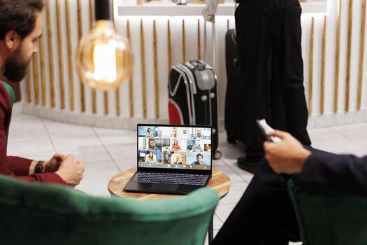Entrepreneurs use videoconference call in hotel lobby, attending online business meeting before doing check in at reception front desk. Businessmen meet with team on telework. photo