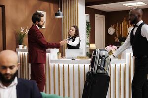 Formal guest fill in registration forms at front desk, doing easy check in process to see room reservation. Businessman travelling for work, receiving great concierge service from staff. photo