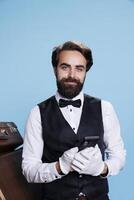 Bellhop leveraging mobile device to browse internet while appearing on camera as an sophisticated representative of an exclusive hotel. Concierge going online and confirming booking requests. photo