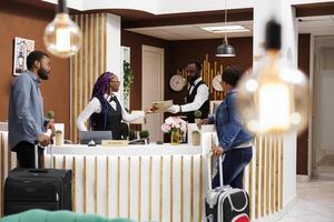 African American couple man an woman standing at hotel reception checking in at reception, waiting for room key or access card. Front desk staff managing guest check-in or check-out process photo