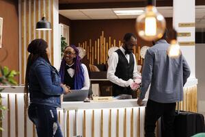 Friendly smiling front desk staff welcoming visitors at reception area of hotel. Smiling African American receptionist giving arriving guests information. People checking in at resort photo