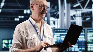 Proactive professional navigating network of server hardware in industrial hub. IT consultant with laptop doing optimizations and maintenance in data center, preventing system errors photo