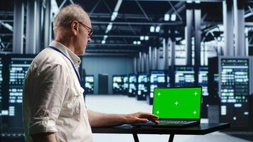 Developer in server room expertly managing data while navigating through industrial mainframes. Expert ensuring flawless cybersecurity guard, optimizing systems using green screen laptop photo