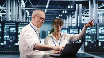 Competent workers looking around high tech data center, using laptop to crosscheck disaster recovery plan and assess server gadgets in need of replacement, preventing flaws photo