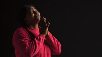 Graceful black woman gazing upwards with palms extended in gesture of reverance and adoration. Side-view portrait of african american lady engaged in prayerful reflection in isolated background. photo