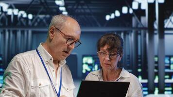 Efficient technical support executives looking around server hub, using laptop to crosscheck disaster recovery plan and assess mainframes in need of replacement, preventing hazards photo