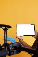 Close-up shot of tablet with isolated chromakey template carried by african american female cyclist. In front of yellow background, a black person is holding a device displaying blank whitescreen. photo