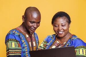 Cheerful black man and woman with smile on face using laptop and enjoying internet leisure activity together. Smiling couple using portable computer, checking information online photo