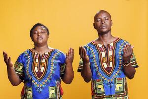 African american couple praying and asking blessing while posing with arms wide open. Religious man and woman prayers pair with closed eyes spreading hands and pleading god photo