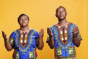 africano americano Pareja Orando y preguntando bendición mientras posando con brazos amplio abierto. religioso hombre y mujer oraciones par con cerrado ojos extensión manos y Suplicando Dios foto