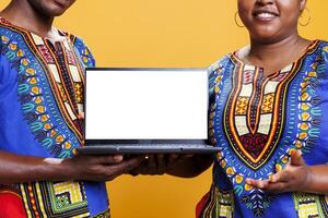 Man and woman promoting laptop blank screen with copy space for software advertising. African american couple showing with empty white display for app promo mockup closeup photo
