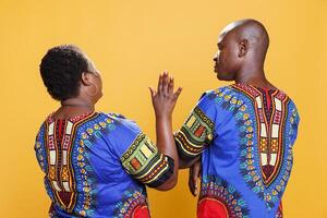 Woman rising hand up while chatting with man back view. African american couple wearing ethnic clothes speaking, girlfriend showing interrupting gesture while boyfriend talking photo