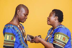 Woman holding open empty wallet with no finance and shouting at unhappy husband. African american couple having conflict while discussing financial problem and displaying purse with no money photo