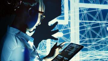 Capable supervisor overseeing dimly lit server hub, running code on tablet, doing checkup on technologically advanced machines clusters made of servers, networking systems and storage arrays photo