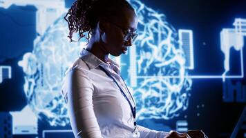 African american woman writing artificial intelligence script code in startup workspace on laptop terminal. Hardworking employee doing maintenance work in high tech facility updating AI systems photo