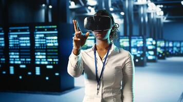 African american woman immersed in virtual reality at data center, doing equipment maintenance. Qualified engineer using VR headset to optimize server equipment performance, checking operations photo