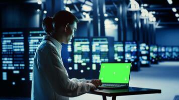 IT consultant running code on chroma key laptop, troubleshooting data center equipment. Cloud computing business executive using green screen device to examine servers and networking systems photo