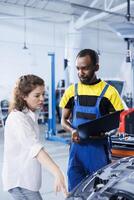 Smiling serviceman in car service uses tablet to calculate invoice after fixing broken automobile radiator. Specialist uses device to inform customer of final costs after mending vehicle photo