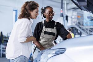 Mechanic at auto repair shop conducts annual vehicle checkup, informing customer about needed compressor belt replacement. Adept garage worker talks with customer after finishing car inspection photo