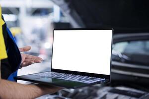 Trained repairman in garage using mockup laptop to follow checklist while doing maintenance on customer car. Precise specialist in repair shop does checkup on client vehicle helped by isolated screen device photo