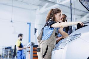 Efficient mechanic at auto repair shop conducts annual vehicle checkup, informing client about needed engine replacement. Automotive expert talks with customer after finishing car maintenance photo