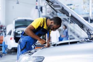 ingeniero expertamente examina coche frenos utilizando avanzado mecánico herramientas, asegurando óptimo automotor actuación y seguridad. bipoc con licencia garaje empleado conduce anual vehículo chequeo foto