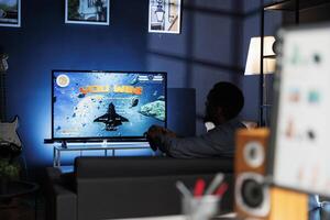 African american guy embraces tourney triumph after winning online gaming contest. Young participant has fun with simulated long range firearms, winning space shooting tournament. photo