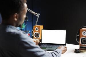 African american freelancer examines white screen on laptop, working from home and using blank chromakey display on wireless computer. Independent contractor looks at copyspace layout. photo