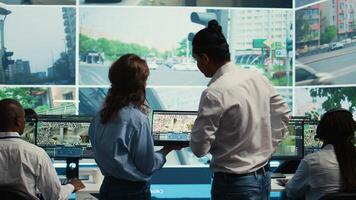 Diverse team following city traffic on a display in monitoring room, reviewing CCTV satellite radar footage. Employees working on surveillance and data collecting, control center. Camera B. photo