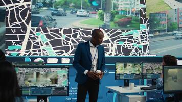 Supervisor arriving in the control center at shipping agency, overseeing main gps locating activities to ensure order and parcel delivery. Diverse employees working with satellite maps. Camera B. photo