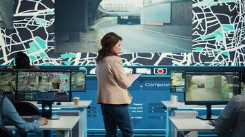 Manager supervising diverse employees operators in delivery call center office, people using global positioning system to guide shipment cars on city routes via satellite navigation map. Camera B. photo