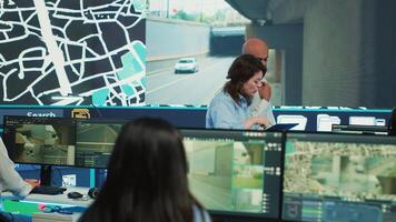 Diverse team of agency employees following delivery trucks via gps coordinates, working with CCTV surveillance footage and satellite map to ensure order shipping. Monitoring room. Camera A. photo