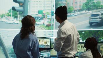 Diverse team following city traffic on a display in monitoring room, reviewing CCTV satellite radar footage. Employees working on surveillance and data collecting, control center. Camera A. photo