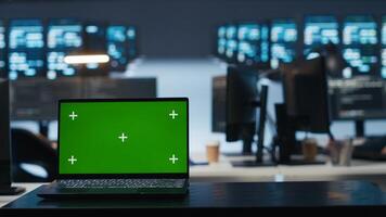 Focus on isolated screen laptop in data center with man in blurry background coding, managing server rows. Close up shot of chroma key notebook and IT expert overseeing rackmounts operating data photo