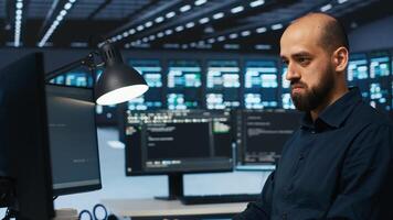 System admin focused on programming in server farm housing advanced equipment storing massive datasets. Developer typing code on PC to mend data center racks doing complex computational operations photo
