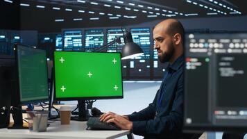 Technician overseeing server room, running code on green screen computer, troubleshooting servers. Software developer upgrading hardware clusters and storage arrays using mockup PC monitor photo