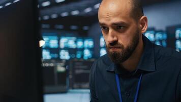Overworked engineer feeling stressed while coding in data center facility, trying to ensure optimal performance of supercomputers. Tired man feeling fatigued while using PC to monitor server cabinets photo