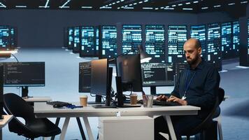 Experienced person typing code on computer monitors in high tech facility with server rows providing computing resources. IT professional overseeing rackmounts operating data photo
