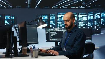 System administrator overseeing server room, running code on PC, troubleshooting rigs. Software expert upgrading hardware clusters, networking systems and storage arrays, panning shot photo