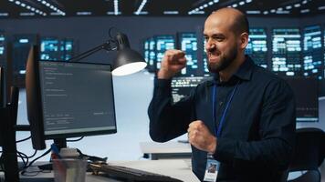 Hardworking engineer feeling happy and celebrating after being able to repair damages in data center facility. Cheerful man pleased after using PC to fix server cabinets errors photo